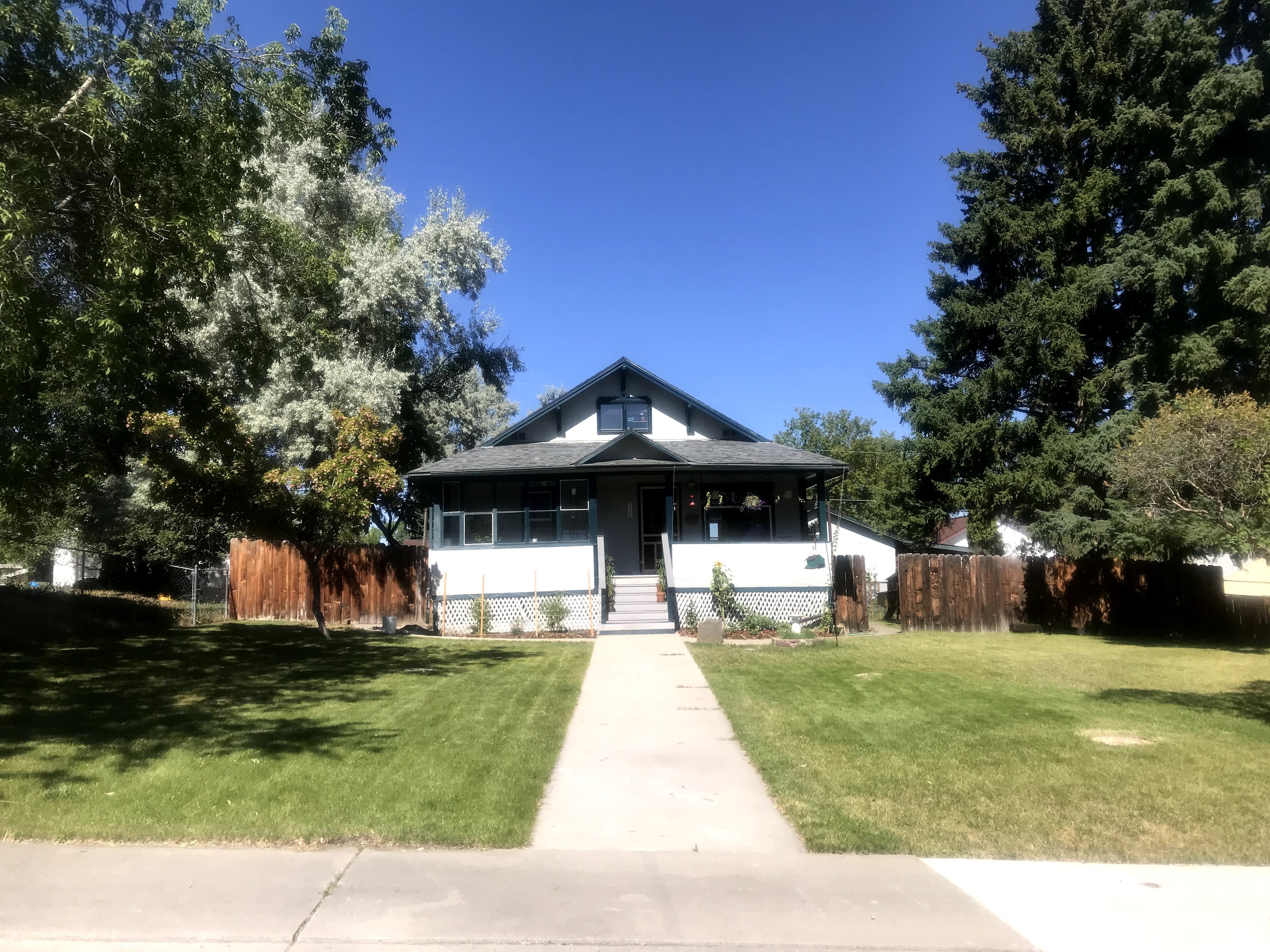 Stucco bungalow with large, empty front lawn and some small plantings.