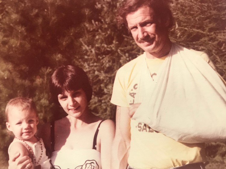 A tall man in a sling stands next to a woman holding a baby