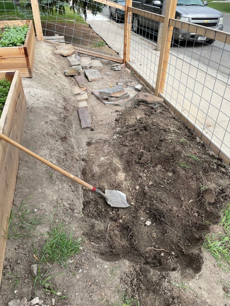 Large dugout area with some stones stacked between a fence and some garden beds