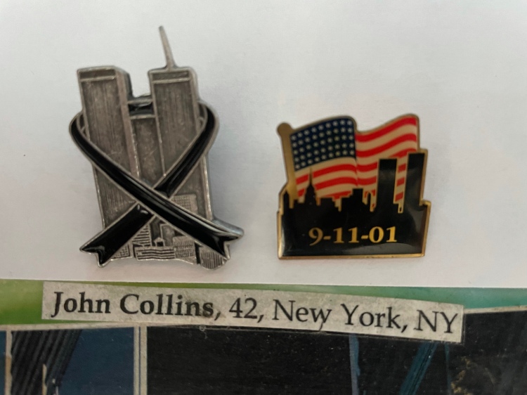 Two commemorative 9/11 pins. The first a pewter World trade Center with a black ribbon. The second the skyline of New York with the Twin Towers set again an American flag background with the date 9-11-01. A slip of paper reading "John Collins, 42, New York, NY."