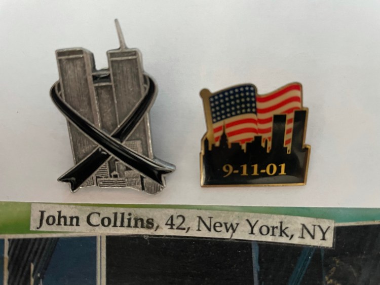 Two commemorative 9/11 pins. The first a pewter World trade Center with a black ribbon. The second the skyline of New York with the Twin Towers set again an American flag background with the date 9-11-01. A slip of paper reading "John Collins, 42, New York, NY."